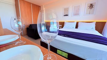 Une chambre d’hôtel avec un lit, une table de chevet sur laquelle se trouvent un verre à vin et une assiette, une commode en bois et une vue sur l’extérieur.