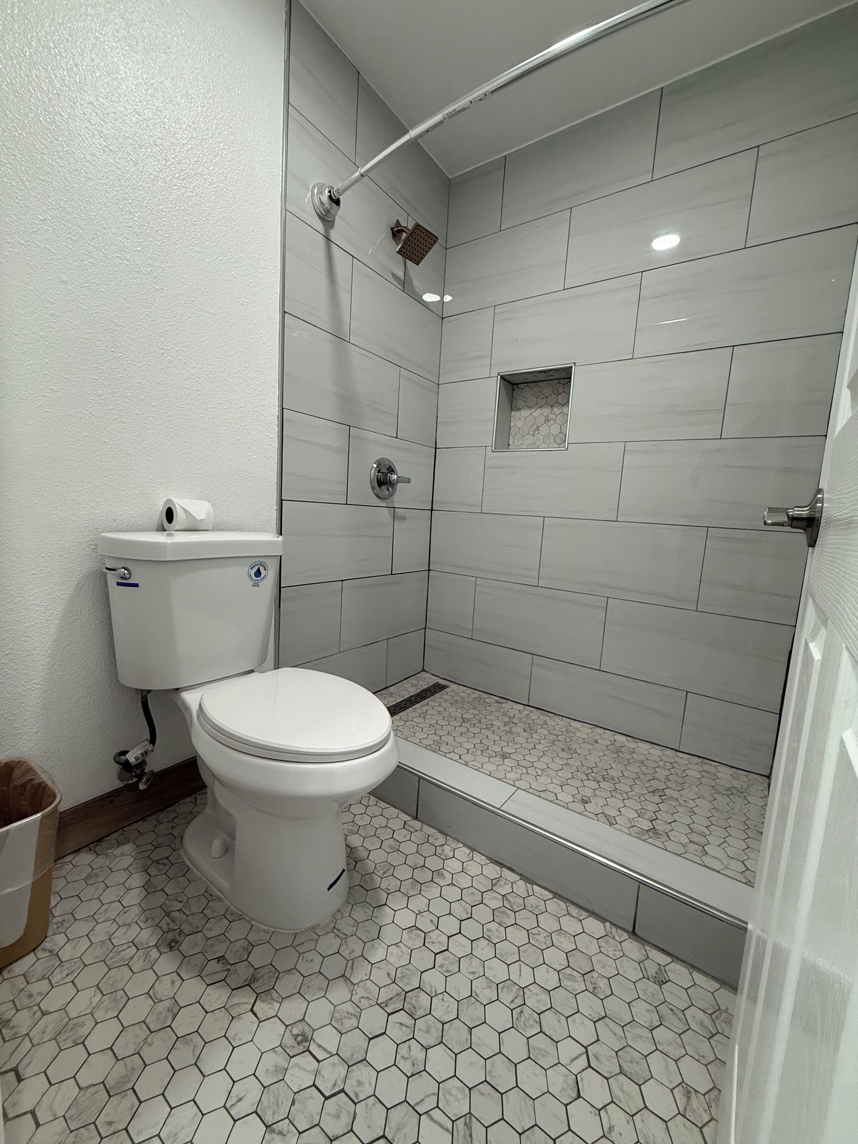 Une salle de bain équipée de toilettes, d’une douche et d’un sol carrelé en forme d’hexagone.
