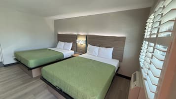 A hotel room with two beds, a wooden headboard, a wall-mounted light, and a built-in shelving unit.