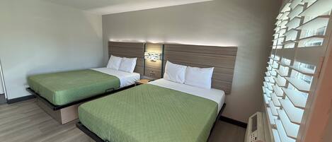 Habitación de hotel con dos camas, cabecera de madera, lámpara fijada a la pared y estantería empotrada.