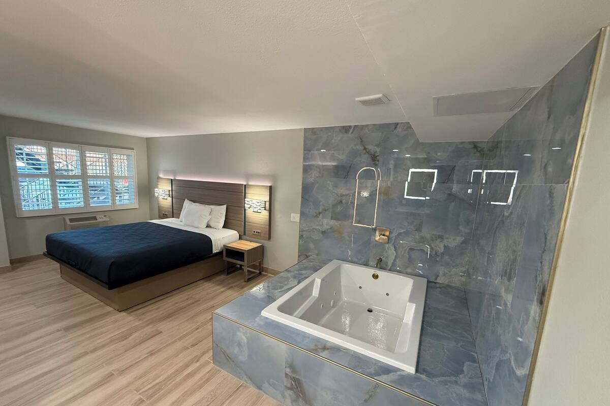 A modern bedroom with a large bed, a built-in bathtub, and a window with a view.