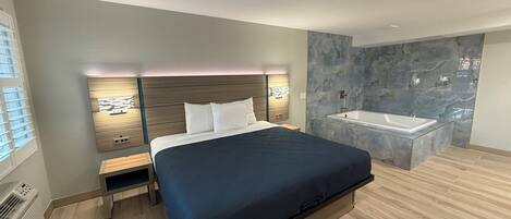 A modern bedroom with a large bed, bedside tables, a built-in nightstand, a wall-mounted light, and a bathroom with a marble wall and a bathtub.