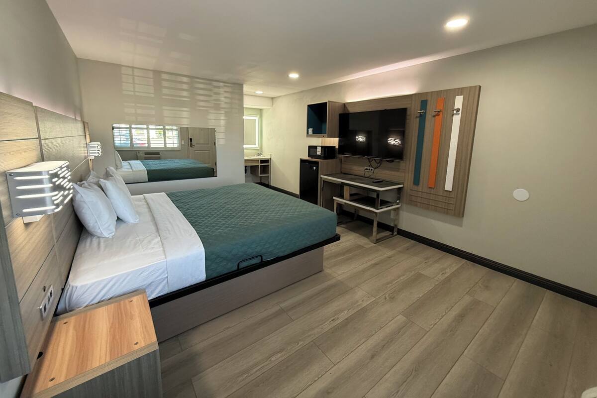 A modern hotel room with a large bed, a desk, a TV, and a small kitchenette.