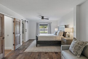 Cozy retreat with a central bed, nightstand, and lamp, plus a ceiling fan and large window with curtains.