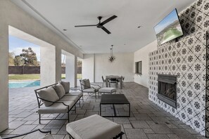 Relax in style with a comfortable outdoor living area featuring a fireplace, flat-screen TV, and pool views.