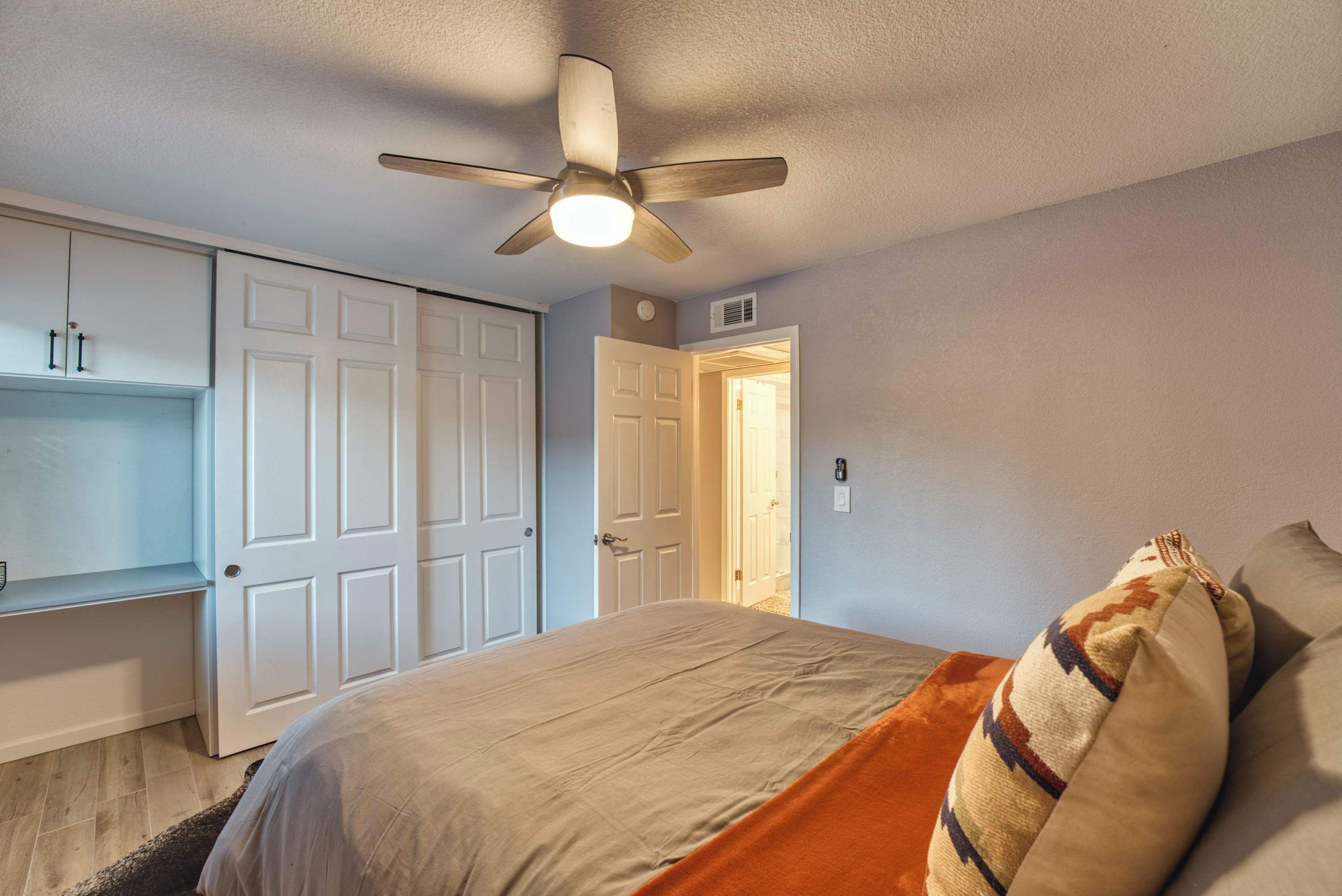 A bedroom with a bed, a ceiling fan, a wardrobe, and a door leading to another room.
