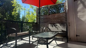Un patio con una mesa, sillas, un paraguas rojo y un muro de ladrillo.