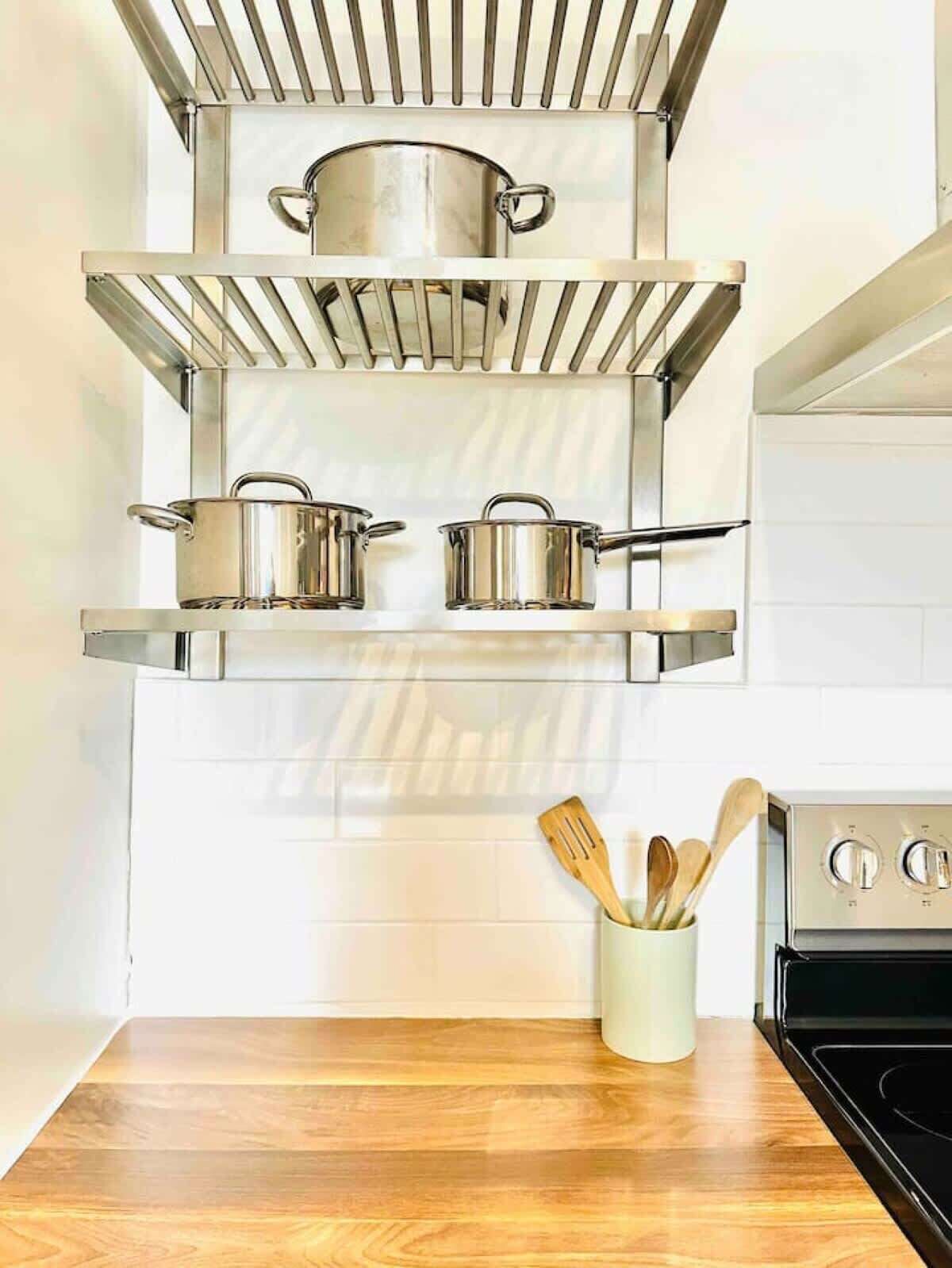 A kitchen with stainless steel shelves holding pots, a wooden spoon holder, and a stove.