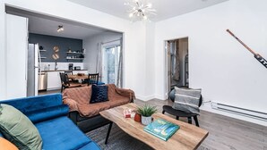 Una sala de estar moderna con un sofá azul, una mesa de centro de madera y una cocina al fondo.