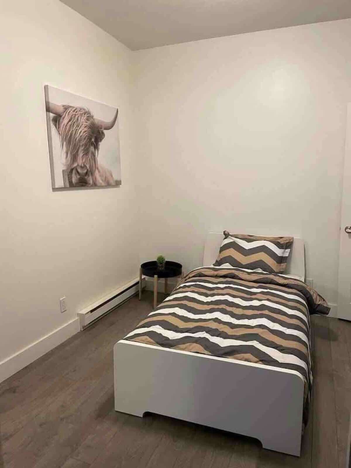 A bedroom with a bed, a nightstand, a wall-mounted picture, and a door.