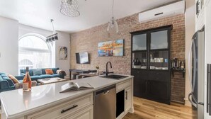 A modern kitchen with a brick wall, a large island with a sink, and a dining area with a sofa and table.