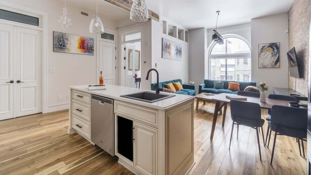 A modern kitchen with a central island, a dining area with chairs, a sofa, and artwork on the walls.