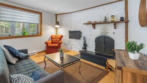 Una sala de estar con sofá, sillón, mesa de centro, chimenea y televisor montado en la pared.