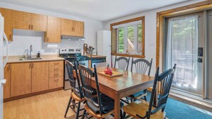 Una cocina con armarios de madera, una mesa de comedor con sillas, lavavajillas y una ventana con vistas a zonas verdes.