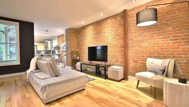 A modern living room with a brick wall, a flat-screen TV, a sofa, a coffee table, and a side table.