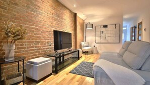 A living room with a brick wall, a flat-screen TV, a sofa, a coffee table, and a lamp.