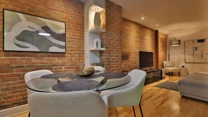 A modern living room with a brick wall, a round glass table, and a flat-screen TV.