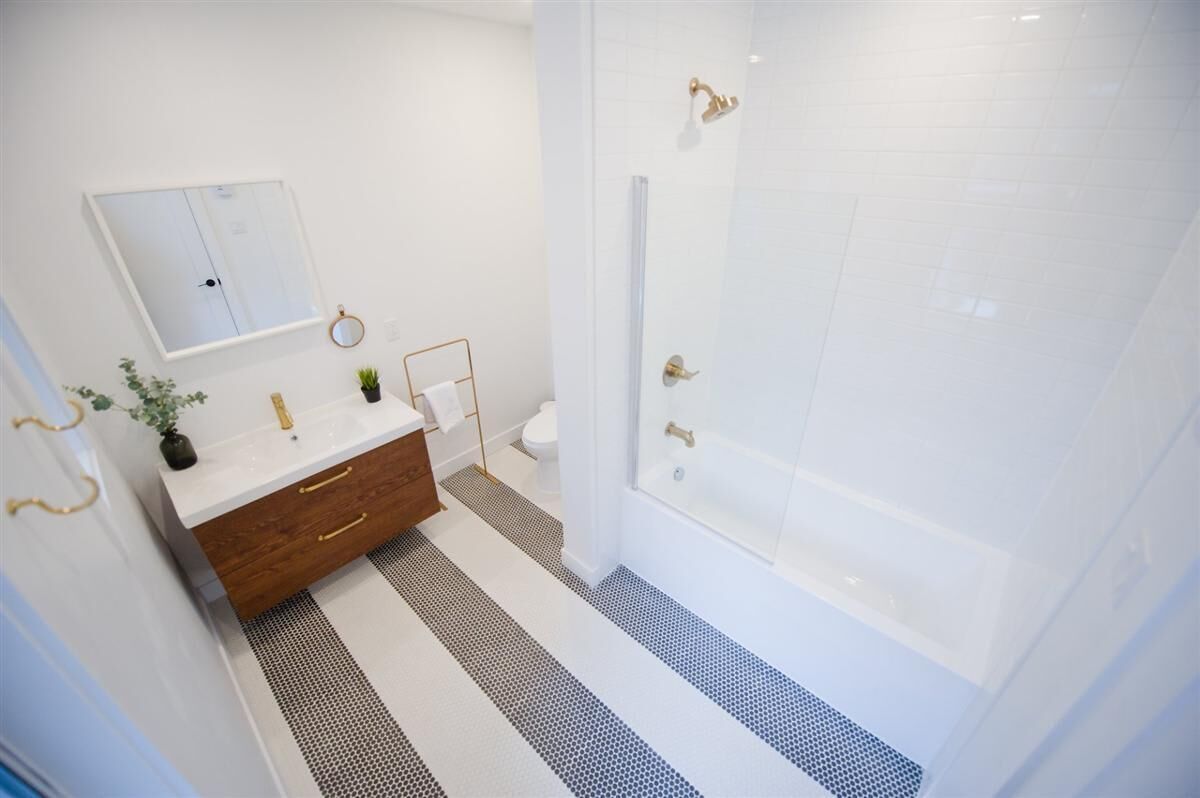 A bathroom with a white vanity, a mirror, a towel rack, a shower with a glass door, and a patterned floor.