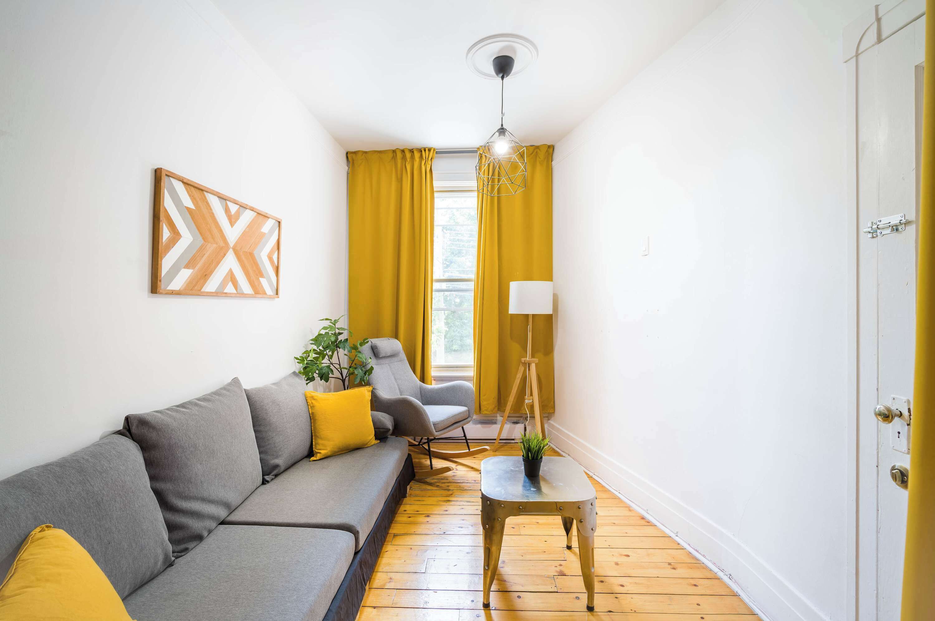 A modern living room with a grey sofa, yellow cushions, a floor lamp, and a geometric wall art piece.
