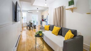 A living room with a sofa, a dining table, and a kitchen in the background. - Trendy 4BR Montreal Home Perfect for Groups (Montréal)