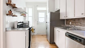 A narrow kitchen with white cabinets, a stainless steel refrigerator, a dishwasher, and a coffee machine. - Walk to Olympic Stadium |Modern Montreal Stay - apartment (Montréal)