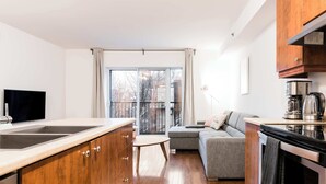 Eine moderne Küche mit Holzausstattung, einem großen Fenster, einem grauen Sofa und einem Essbereich.