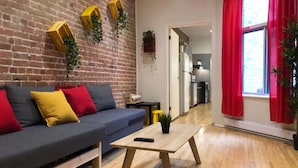 Ein Wohnzimmer mit Backsteinwand, einer Couch mit Kissen, einem Holztisch und einem Fenster mit roten Vorhängen.