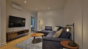 Ein modernes Wohnzimmer mit Flachbildfernseher, einer Couch, einem Couchtisch und einer Stehlampe.