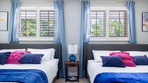 A hotel room with two beds, a nightstand with a lamp, and windows with blinds.