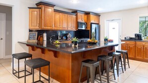 A modern kitchen with wooden cabinets, a large island with stools, and a microwave above the island.