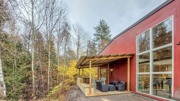 A modern house with a covered patio, large windows, and a forested backdrop.