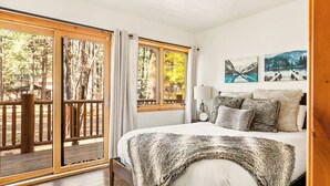 Une chambre avec un grand lit, une terrasse en bois et une vue sur les arbres.