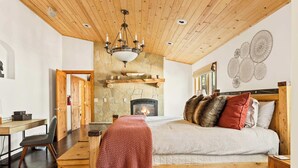 Une chambre confortable avec une cheminée en pierre, un plafond en bois et un lit agrémenté de nombreux coussins.