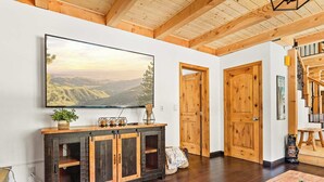 Un vaste salon doté d’un grand téléviseur à écran plat fixé au mur, d’un parquet, d’un meuble en bois avec une façade en treillis et d’un escalier avec des rampes en bois.