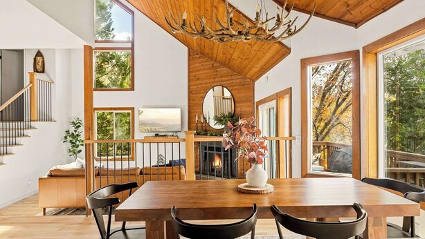 Un amplio comedor con una mesa y sillas de madera, chimenea y ventanas grandes que ofrecen vistas del exterior.