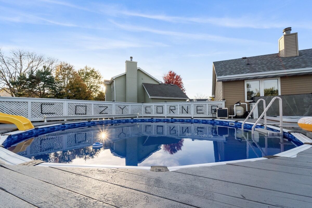 A swimming pool with a wooden deck, surrounded by a metal fence, and a house in the background.