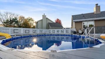 A swimming pool with a wooden deck, surrounded by a metal fence, and a house in the background.