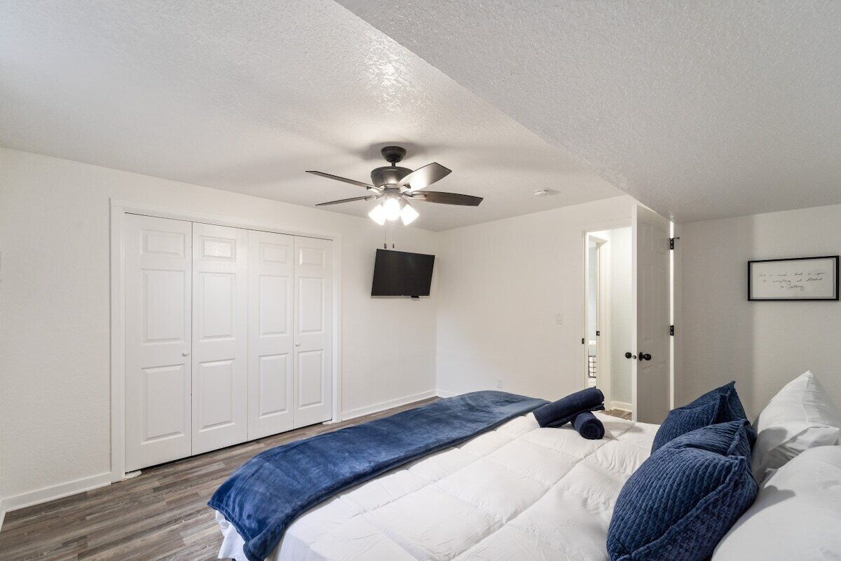 Une chambre à coucher avec un lit, un ventilateur de plafond, un téléviseur fixé au mur et une porte.