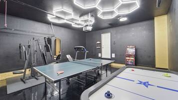 A multipurpose room with a ping pong table, a foosball table, and exercise equipment.