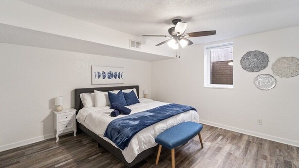 Une chambre à coucher comprenant un lit, une table de chevet, un ventilateur de plafond, une fenêtre et des éléments décoratifs sur les murs.