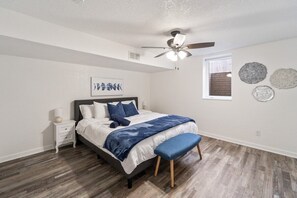 A bedroom with a bed, a nightstand, a ceiling fan, a window, and wall decorations. - Huge Home, Gym, Game Room, Spa, BBQ, Near I-35 (Ankeny)