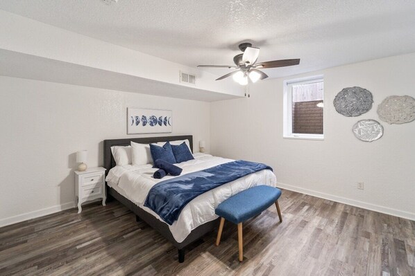 Un dormitorio con cama, mesita de noche, ventilador de techo, ventana y adornos en la pared.