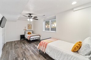 A bedroom with two beds, a ceiling fan, a window, and a television on the wall. - Huge Home, Gym, Game Room, Spa, BBQ, Near I-35 (Ankeny)