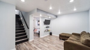 A modern living room with a staircase, a sofa, and a flat-screen TV mounted on the wall.