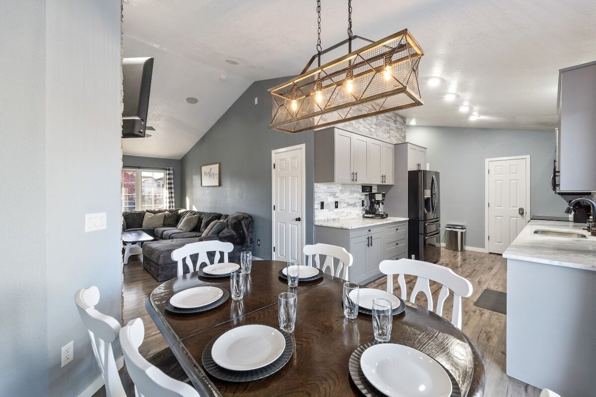 A dining area with a wooden table set for six, white chairs, and a hanging light fixture.