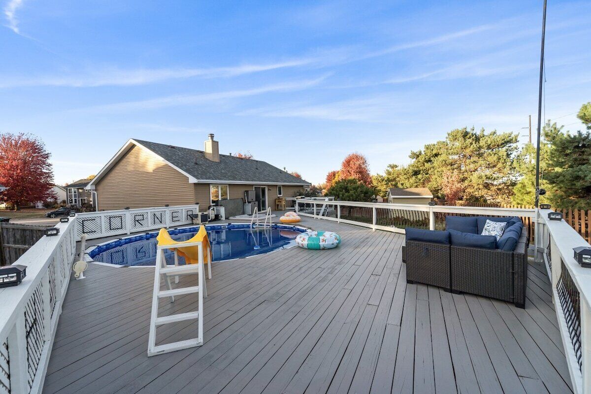 A deck with a swimming pool, a ladder, and outdoor furniture.