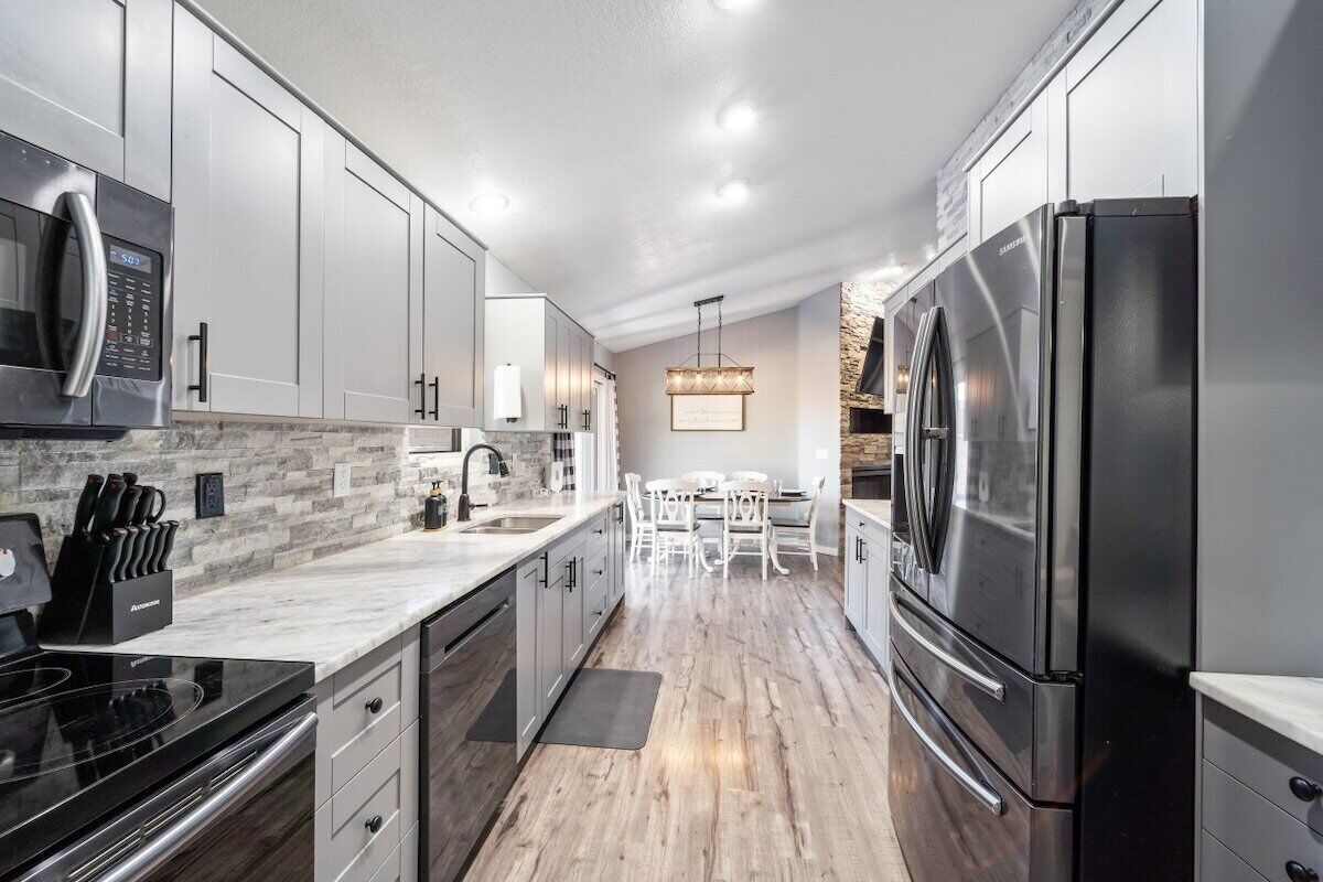 A modern kitchen with stainless steel appliances, white cabinetry, and a stone backsplash.