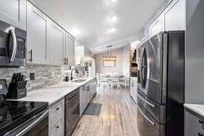 A modern kitchen with stainless steel appliances, white cabinetry, and a stone backsplash. - Huge Home, Gym, Game Room, Spa, BBQ, Near I-35 (Ankeny)