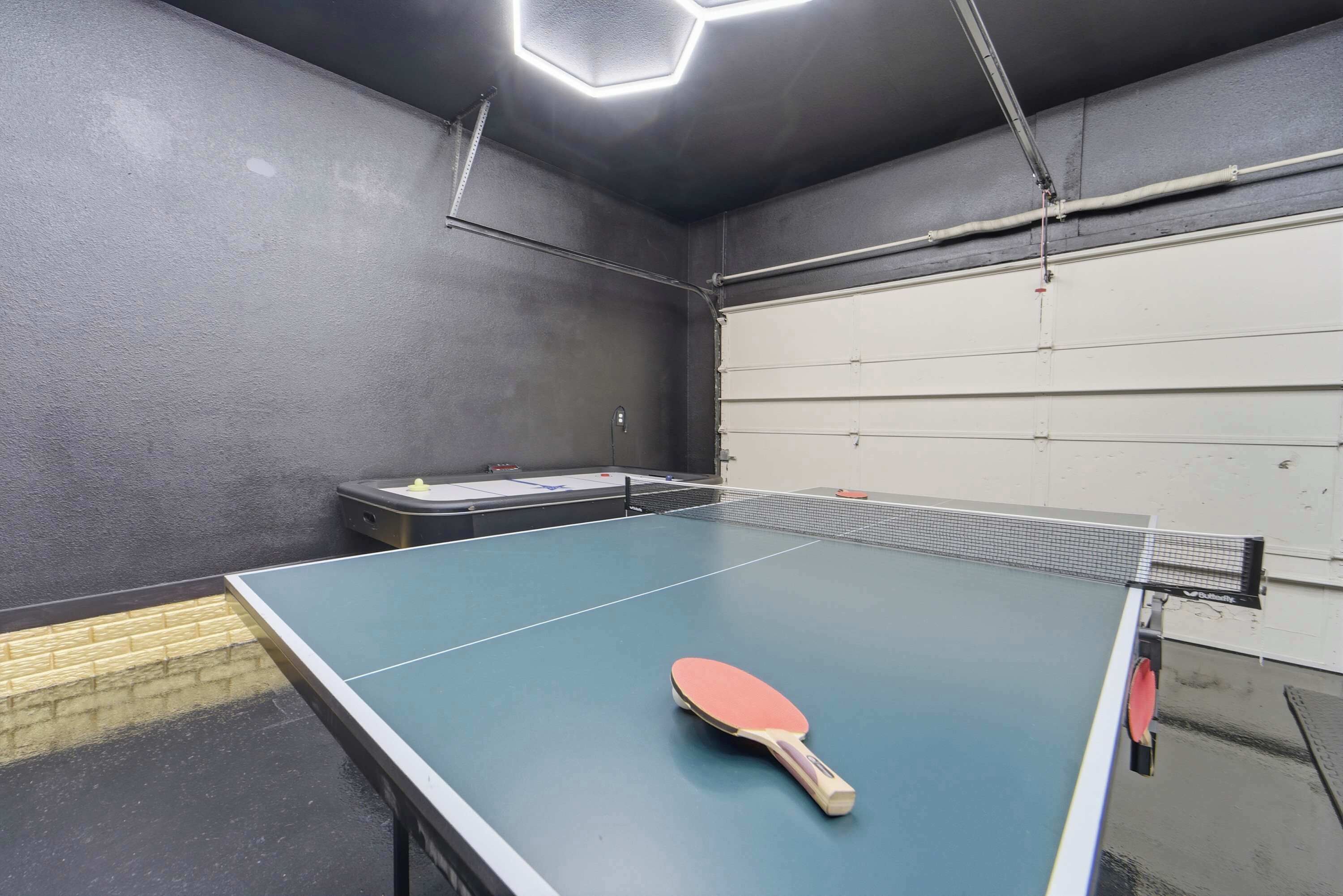 A ping pong table with a paddle in the center, a small table with a laptop, and a white door in the background.