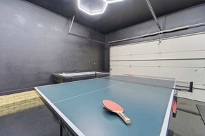 A ping pong table with a paddle in the center, a small table with a laptop, and a white door in the background. - Huge Home, Gym, Game Room, Spa, BBQ, Near I-35 (Ankeny)